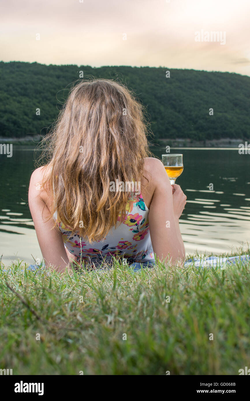 Donna con un bicchiere di vino in riva al lago Foto Stock