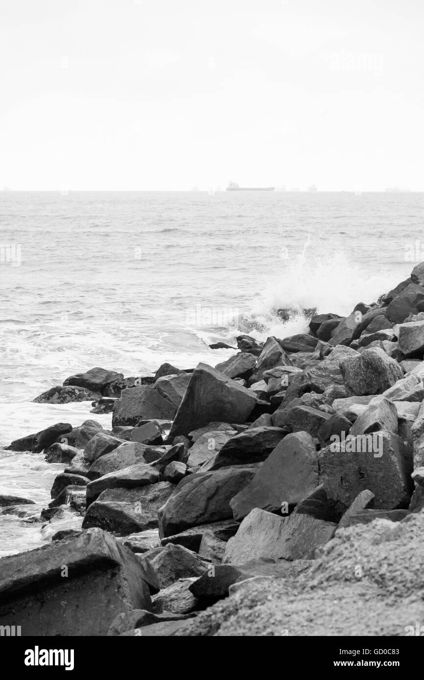 Onde che si infrangono sulla spiaggia rocciosa con nave sullo sfondo Foto Stock