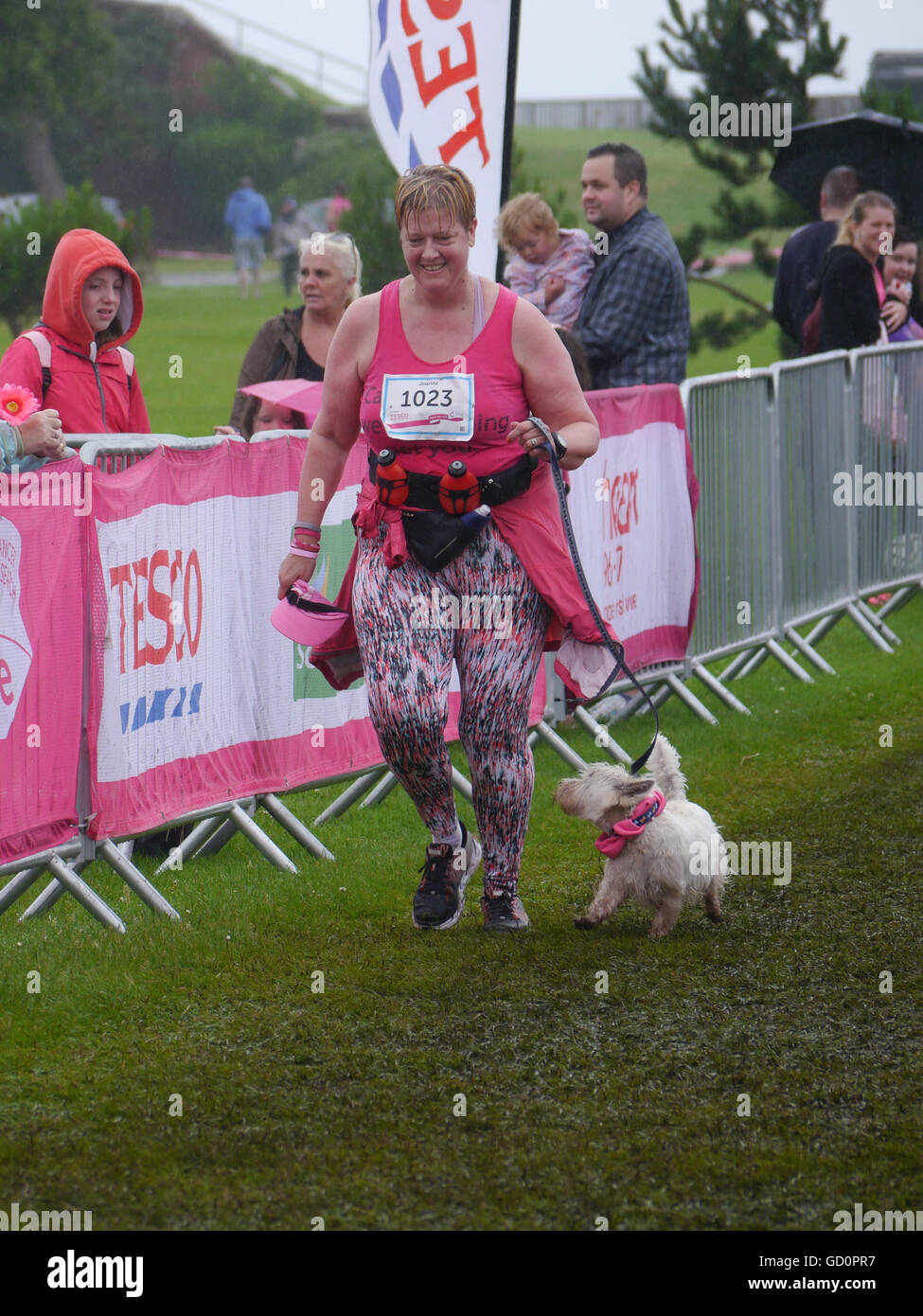 Portsmouth, Hampshire, UK. 10 July 2016. A female crosses the finish line accompanied by her dog during the Race for life. The Race for life is a charity event in which females complete a 10Km or 5Km run in aid of cancer research. Credit:  simon evans/Alamy Live News Foto Stock
