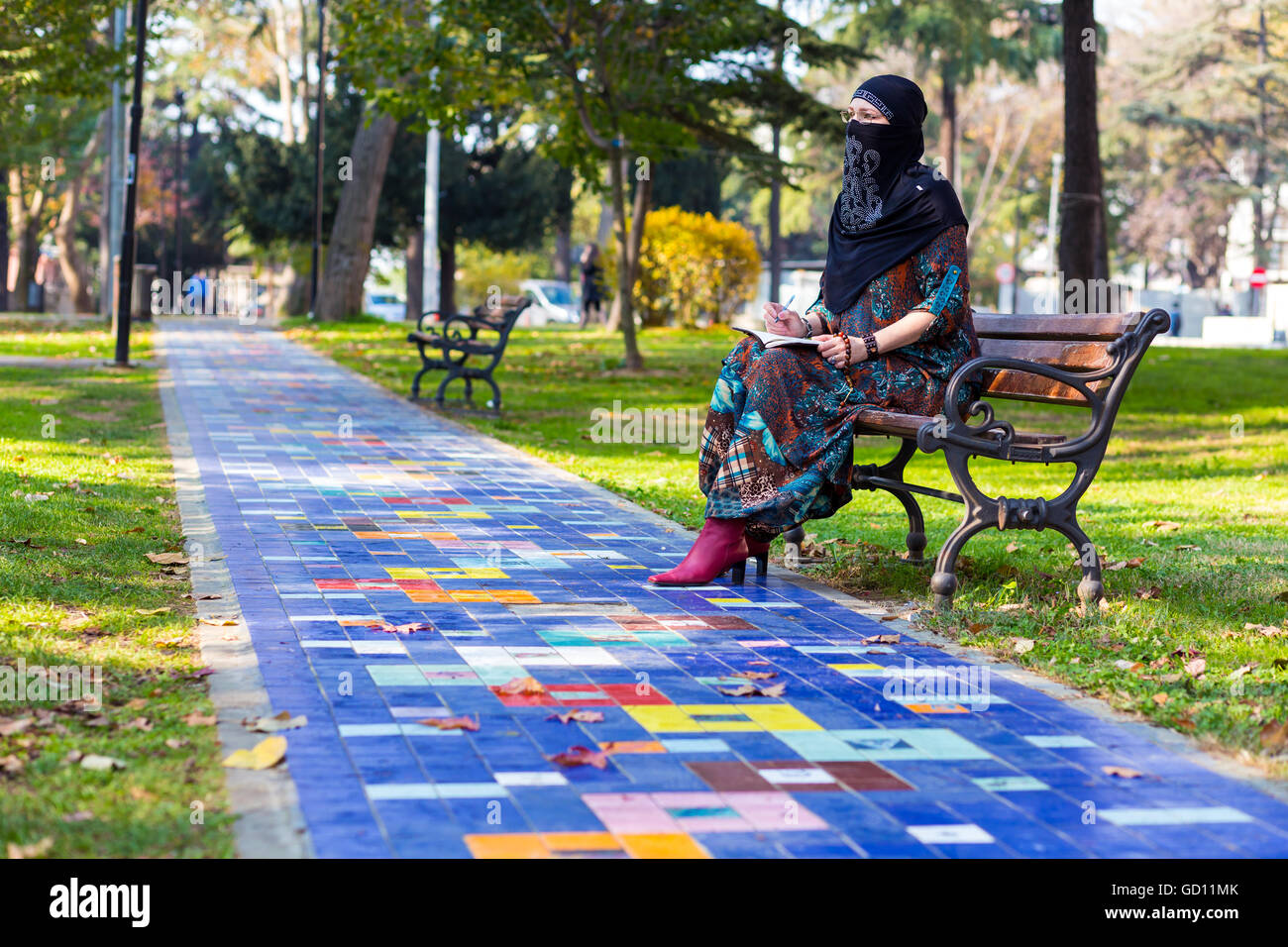 Giovane donna islamica seduto sulla panchina nel parco lungo colorato vicolo lastricato Foto Stock