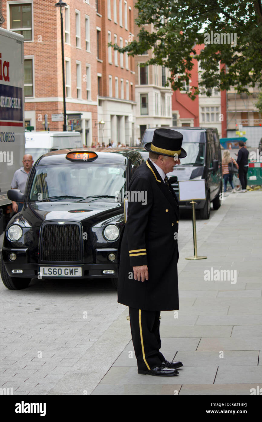 LONDON, Regno Unito - 11 settembre 2015: Concierge al di fuori di un hotel a Londra, con un taxi nero dietro di lui Foto Stock