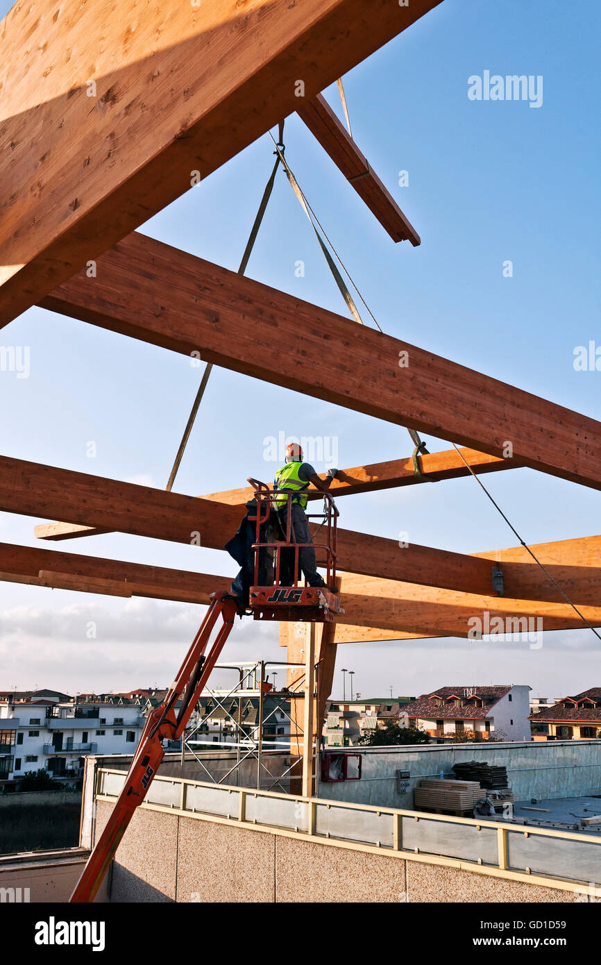 Workman la costruzione di una struttura di telaio di travi lamellari su un cherry picker Foto Stock