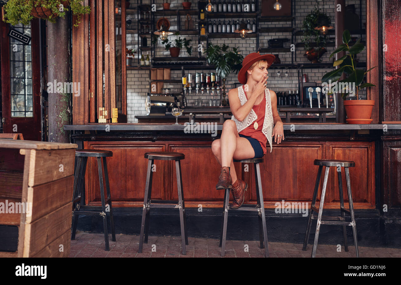 Giovane donna con cappello di fumare in un bar. Azienda di sigarette e di guardare lontano. Foto Stock