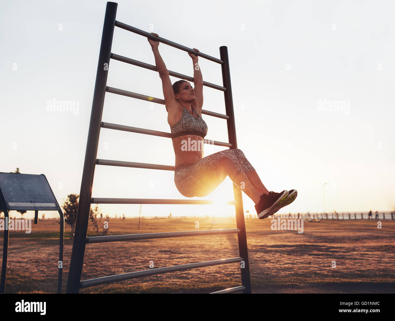 Ritratto di una giovane donna forte appesa alle sbarre a muro con le gambe alzate. donna che fa il fitness che si solleva una gamba sospesa all'aperto. Foto Stock