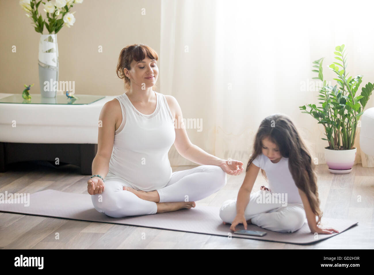 Ritratto di giovane felice yoga in gravidanza la mamma di trascorrere del tempo con la sua piccola figlia, meditando nella posizione del loto con la sua ragazza di capretto Foto Stock