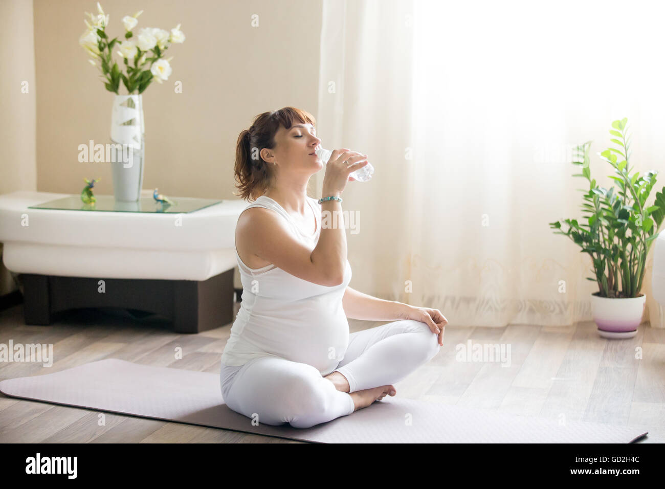 Ritratto di giovane modello gravide di bere acqua fresca con gli occhi chiusi dopo il lavoro nella sala interna. Futura Mamma Foto Stock