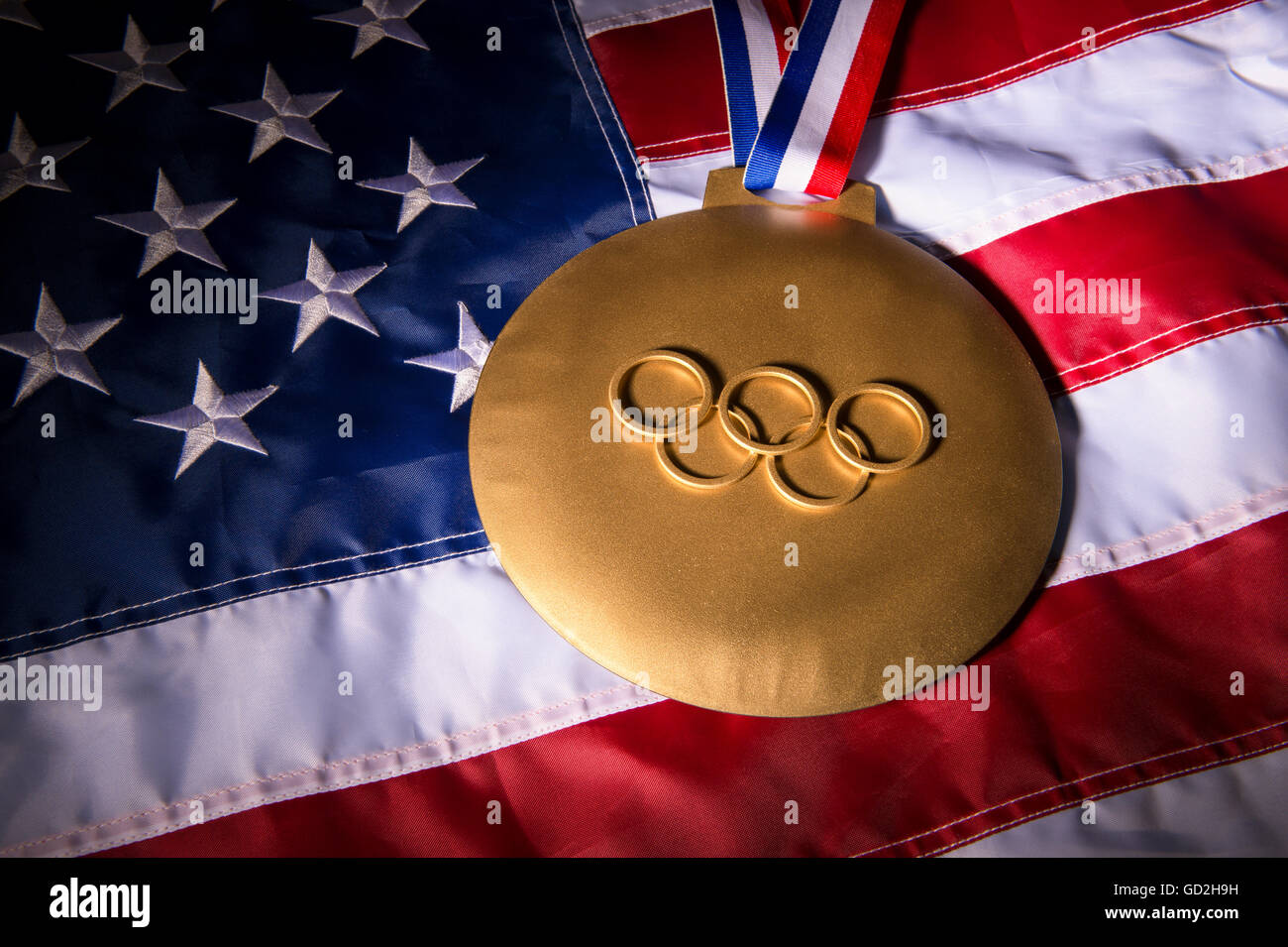 RIO DE JANEIRO - Febbraio 3, 2016: grande medaglia d'oro con anelli olimpici siede sulla bandiera americana sfondo. Foto Stock