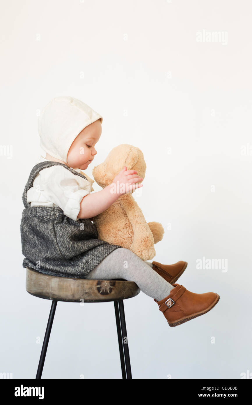 Un giovane bambino, una ragazza seduta su un alto sgabello tenendo un orsacchiotto di peluche. Foto Stock