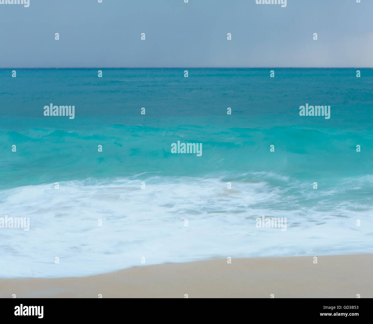 Il mare turchese, le onde che si infrangono sulla spiaggia di sabbia. Foto Stock