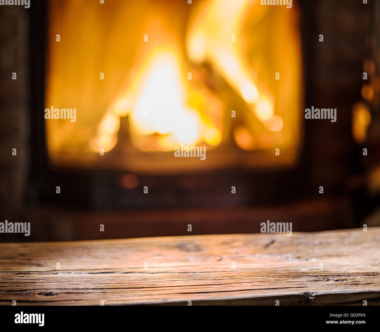 Vecchio tavolo in legno e camino con fuoco caldo sullo sfondo. Foto Stock