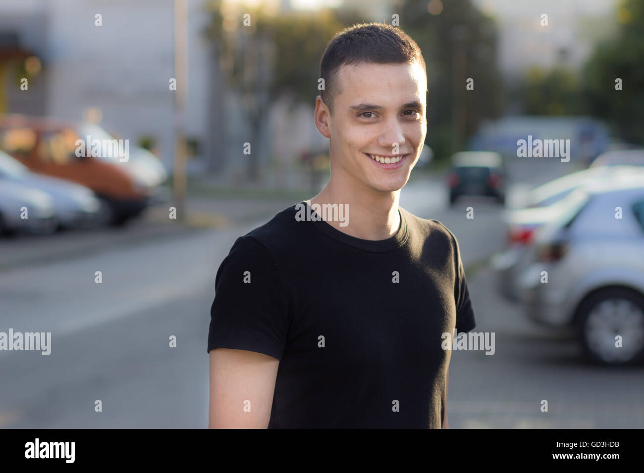 Giovane uomo nei primi 20s sorridente ritratto all'esterno. Profondità di campo e la sfocatura fuori fuoco od sfondo. Foto Stock