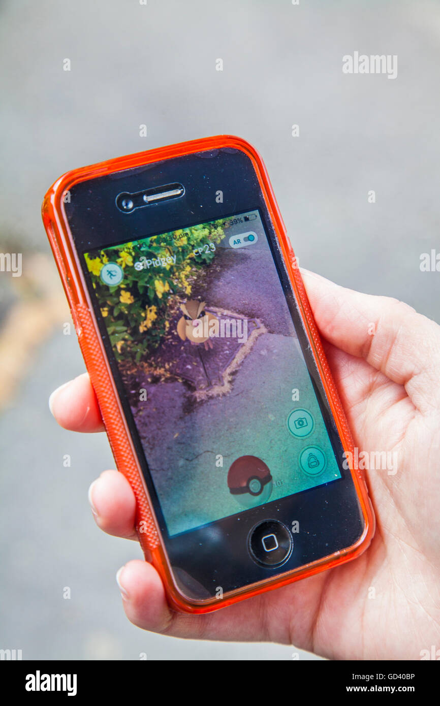 Un giovane persona utilizza un iPhone per giocare Pokémon andare, le ultime realtà aumentata mobile app Game per colpire tutto il mondo mercato app. Foto Stock