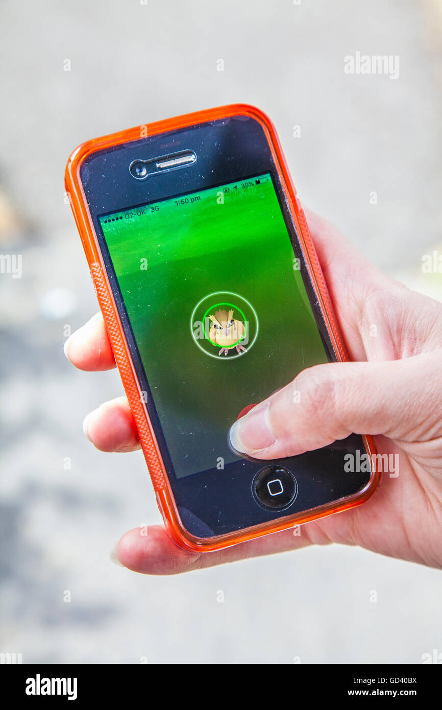 Un giovane persona utilizza un iPhone per giocare Pokémon andare, le ultime realtà aumentata mobile app Game per colpire tutto il mondo mercato app. Foto Stock