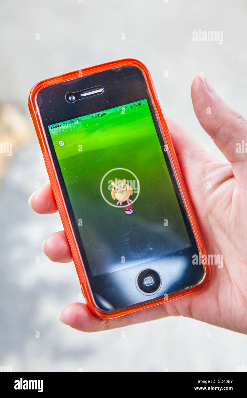 Un giovane persona utilizza un iPhone per giocare Pokémon andare, le ultime realtà aumentata mobile app Game per colpire tutto il mondo mercato app. Foto Stock