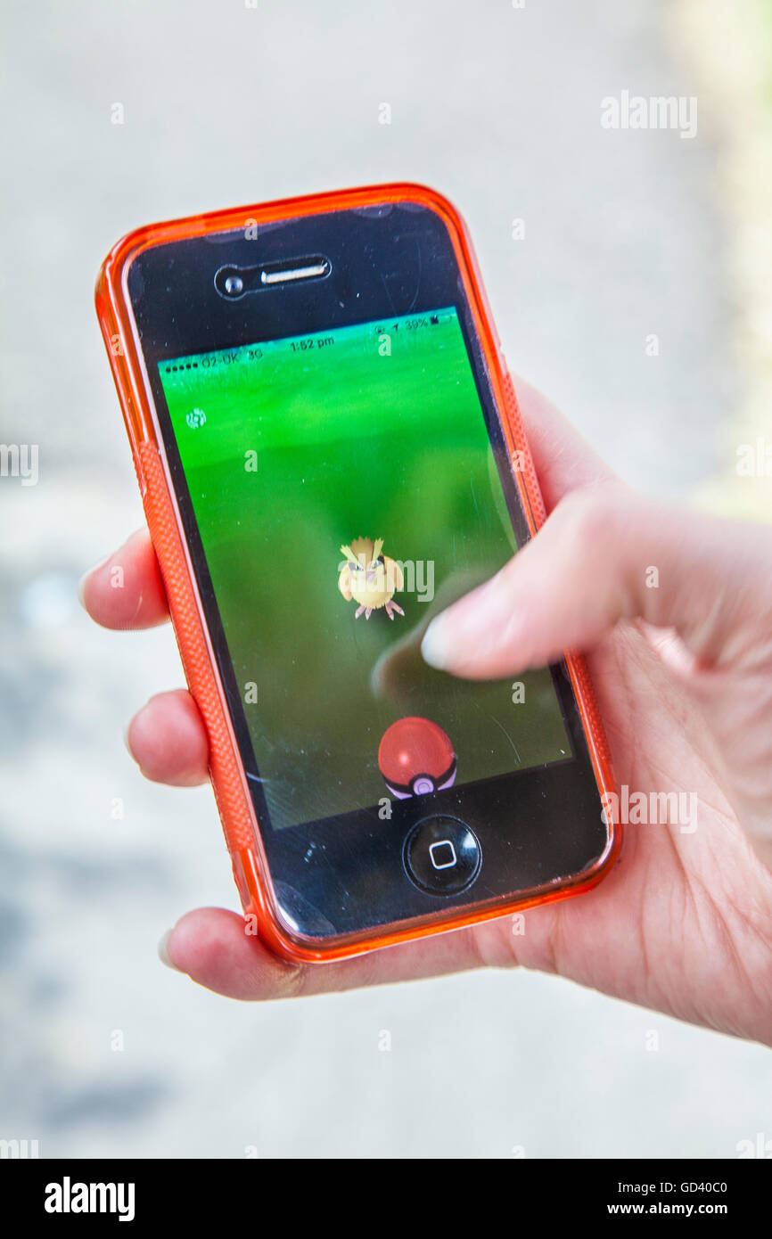 Un giovane persona utilizza un iPhone per giocare Pokémon andare, le ultime realtà aumentata mobile app Game per colpire tutto il mondo mercato app. Foto Stock