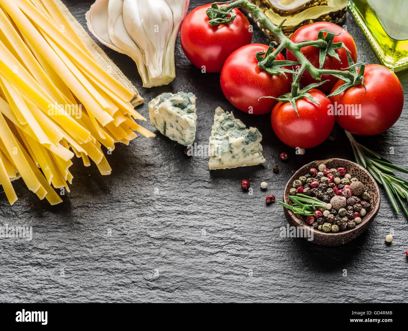 Ingredienti per la pasta. Cherry-pomodori, spaghetti, rosmarino e spezie su una scheda di grafite. Foto Stock
