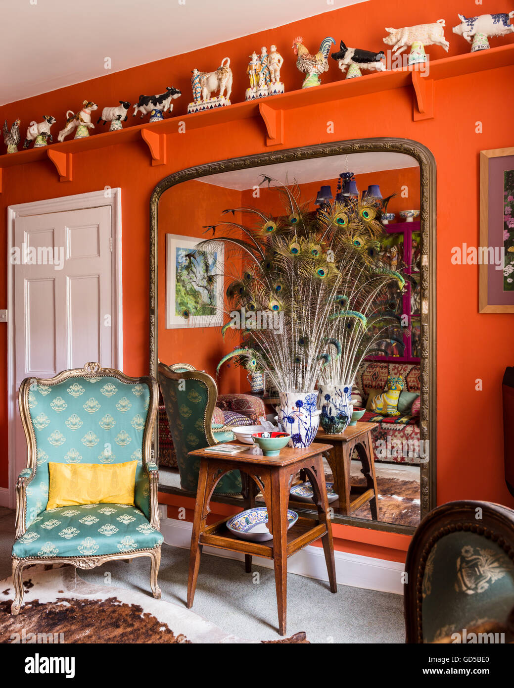 Una collezione di Staffordshire figure lungo scaffale in alto nella camera con retro alato poltrona e vaso di penne di pavone. Foto Stock