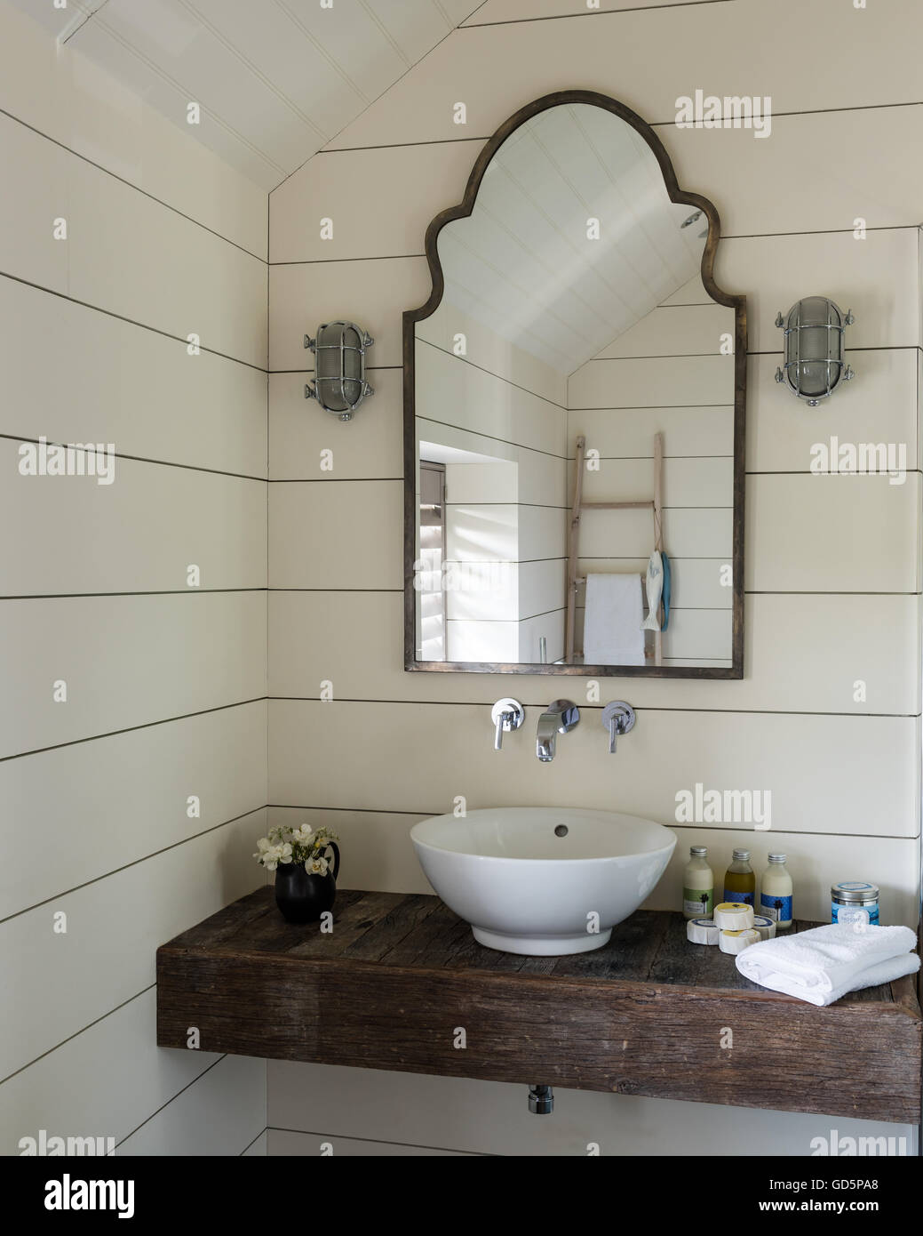 Bacinella in appoggio sulla lastra di legno in bagno con pareti rivestite dipinte di bianco e pannelli a specchio vintage Foto Stock