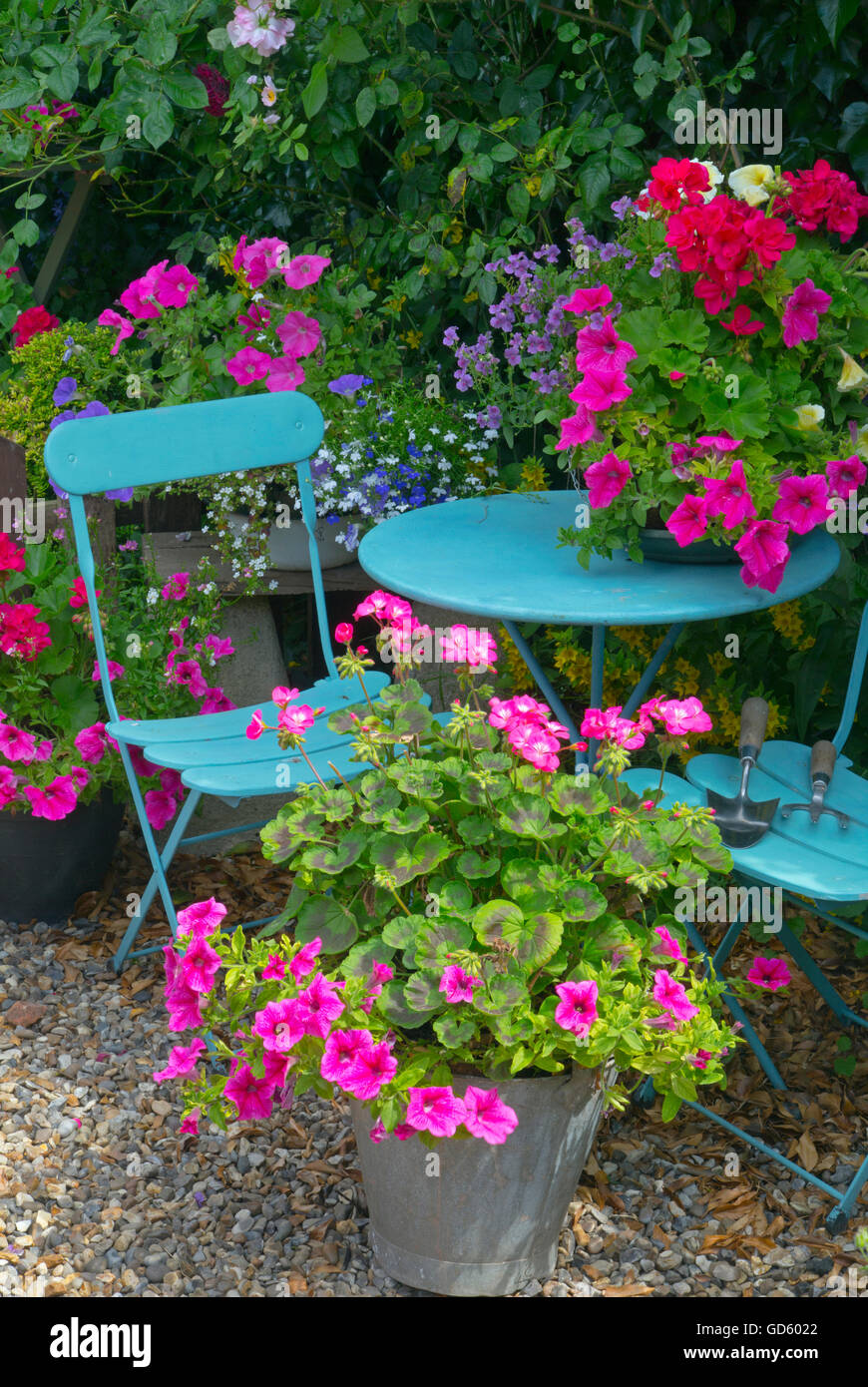 Grazioso giardino cottage con contenitori di fiori blu e tavolo e sedie Foto Stock