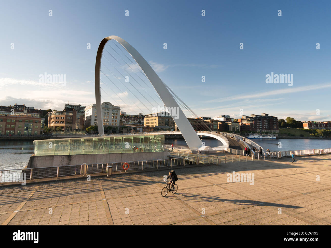 Un ciclista getta una lunga ombra come egli lascia a Gateshead Millennium Bridge sul fiume Tyne, Tyne and Wear, England, Regno Unito Foto Stock