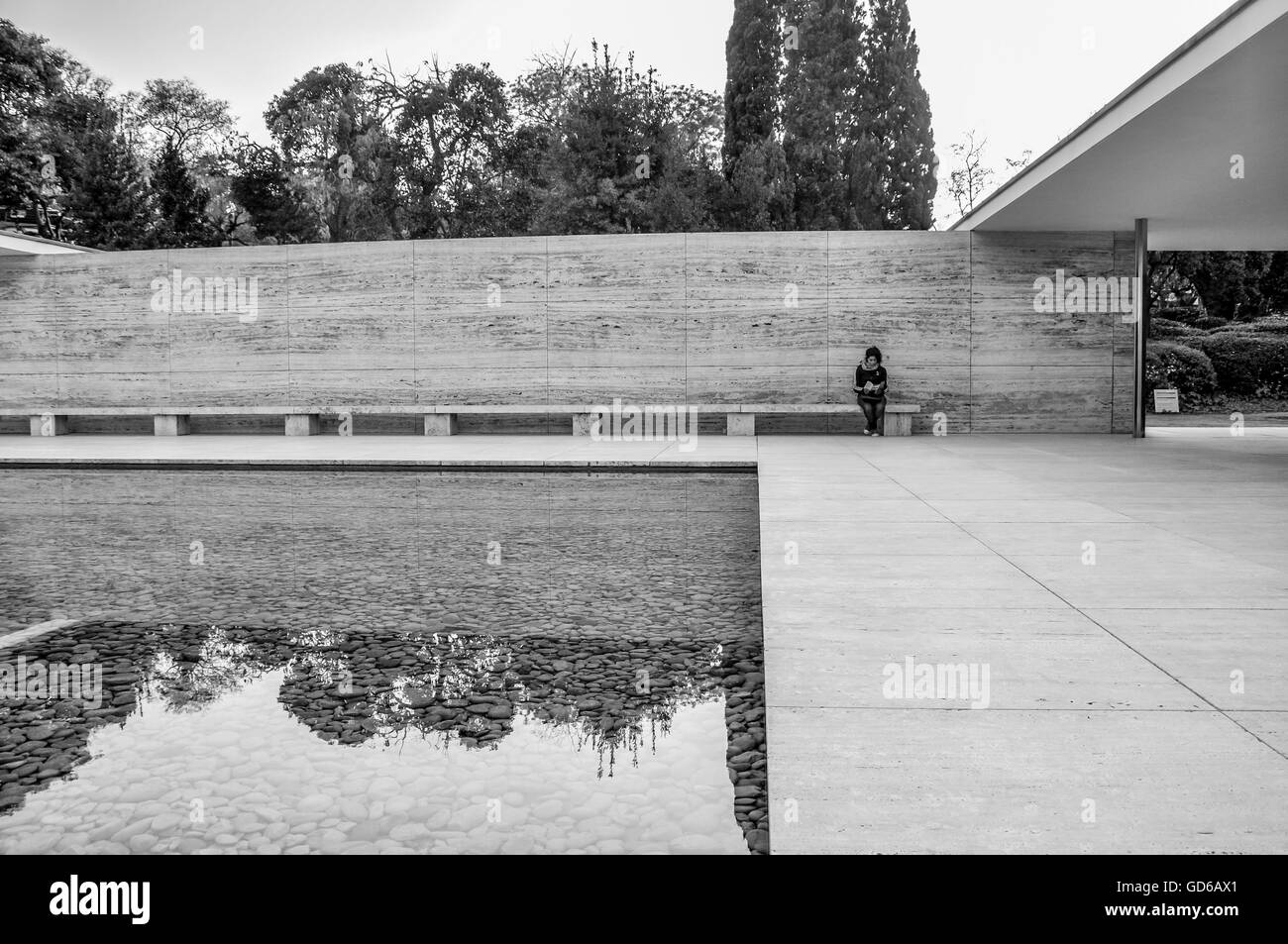 La singola persona seduta sul banco a Barcelona Pavilion con calma piscina riflettente in primo piano Foto Stock