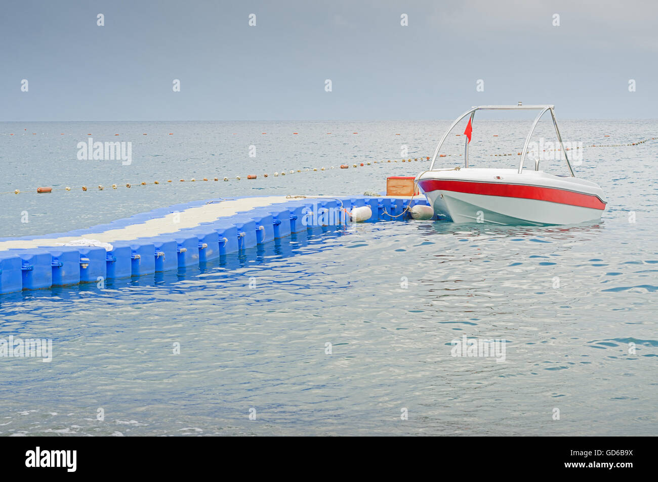 Barca con bandiera rossa parcheggio nei pressi di plastica blu pontoon bridge in attesa per i turisti nel mare Mediterraneo. Foto Stock