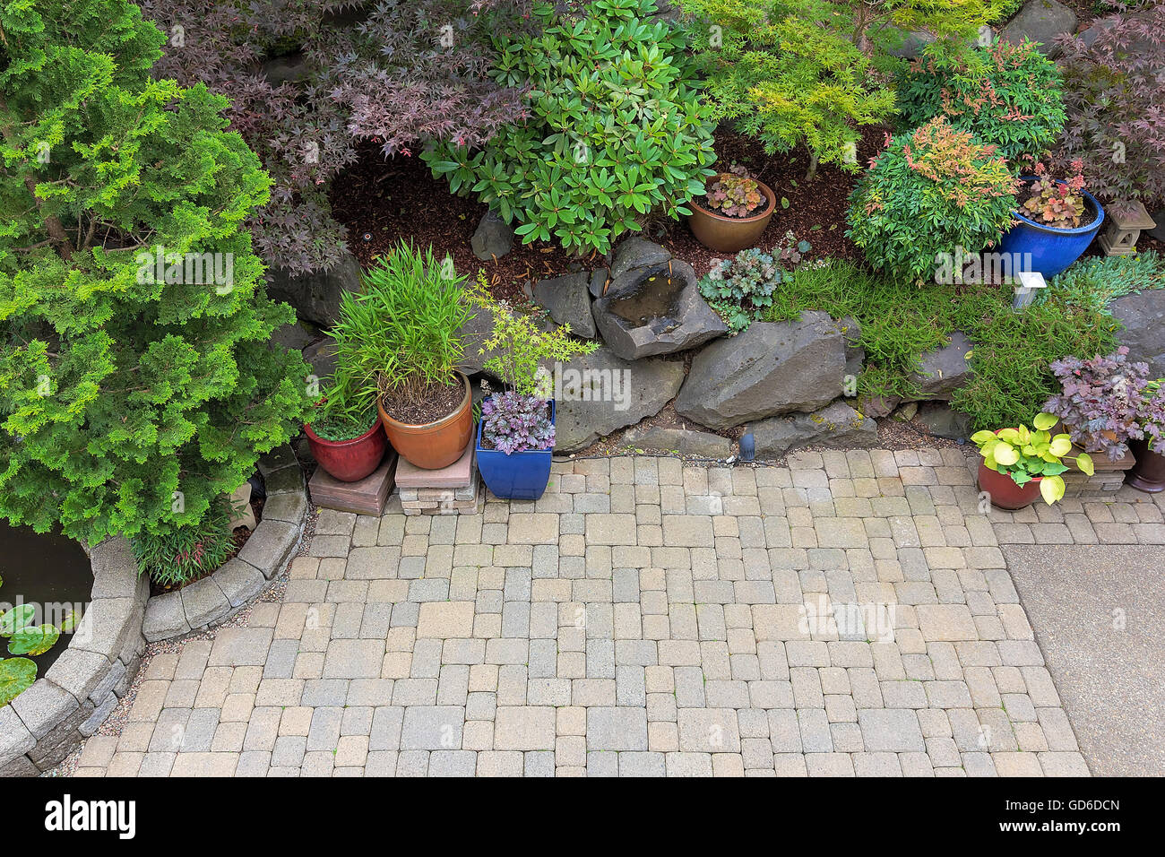 Giardino nel cortile paesaggistico con lastricatore mattoni patio hardscape alberi di piante in vaso arbusti stagno rocce e arredamento Foto Stock