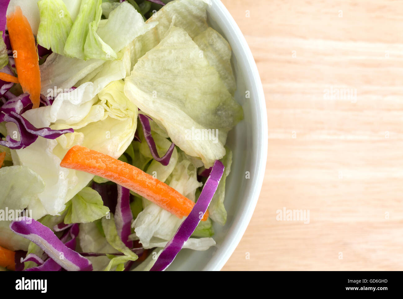 Top vista ravvicinata di una ciotola riempita con le carote affettate, cavolo tagliato a listarelle e lattuga su una tavola di legno top illuminato con l naturale Foto Stock