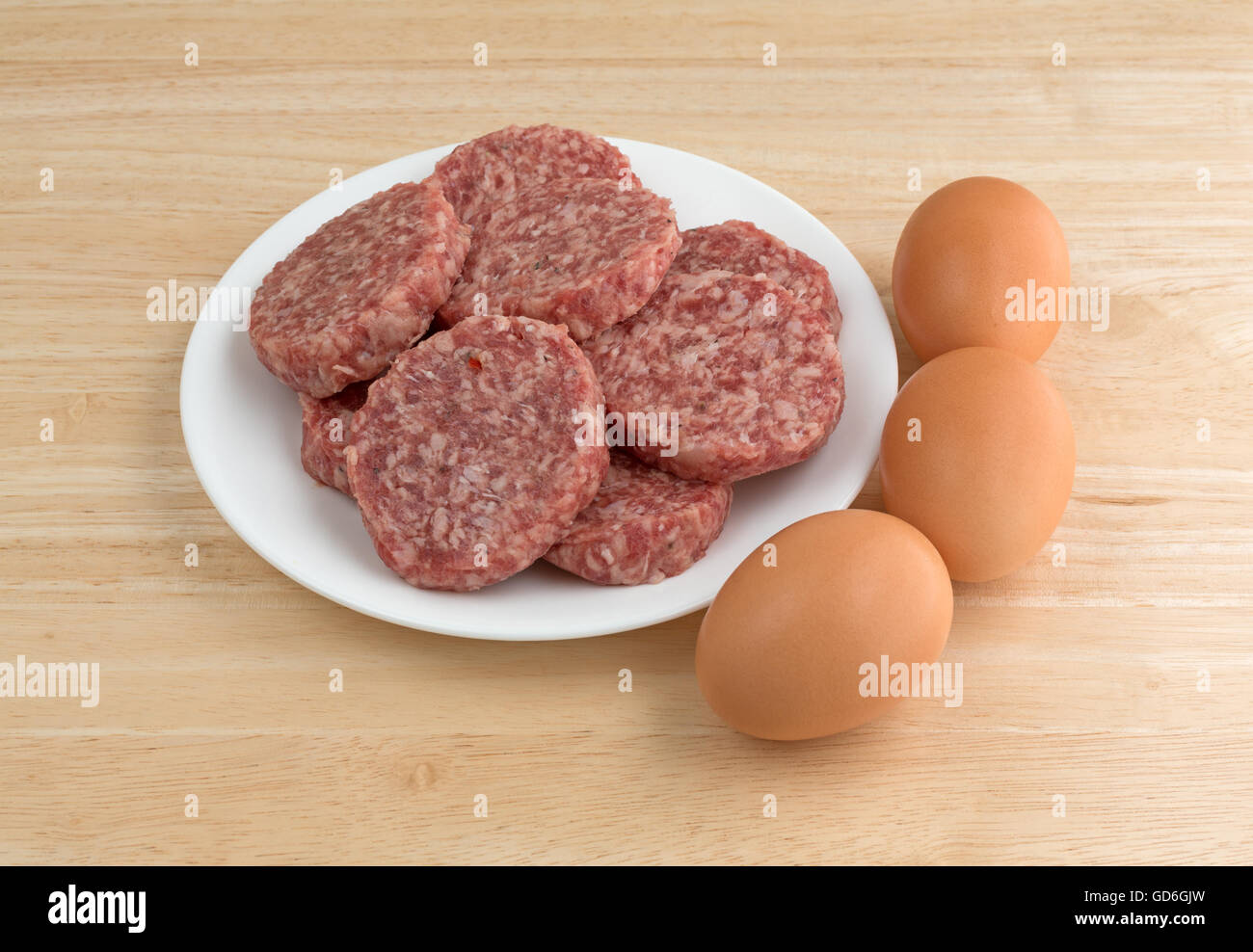 Una piastra bianca con salsiccia polpette e uova a lato sulla cima di un contatore di legno alto. Foto Stock