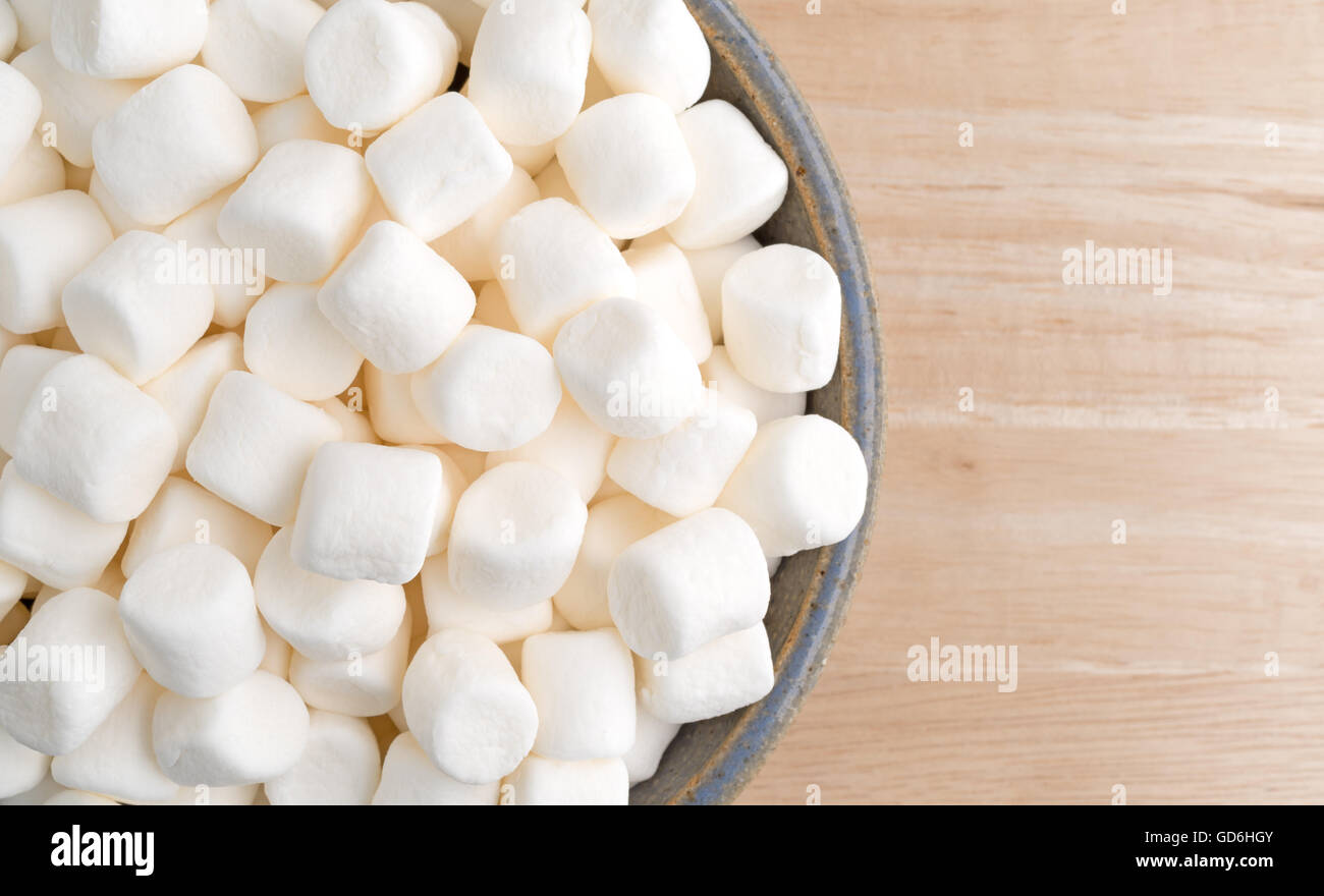 Top vista ravvicinata del piccolo morso dimensioni marshmallows il riempimento di un vecchio recipiente di ceramica su una tavola di legno. Foto Stock