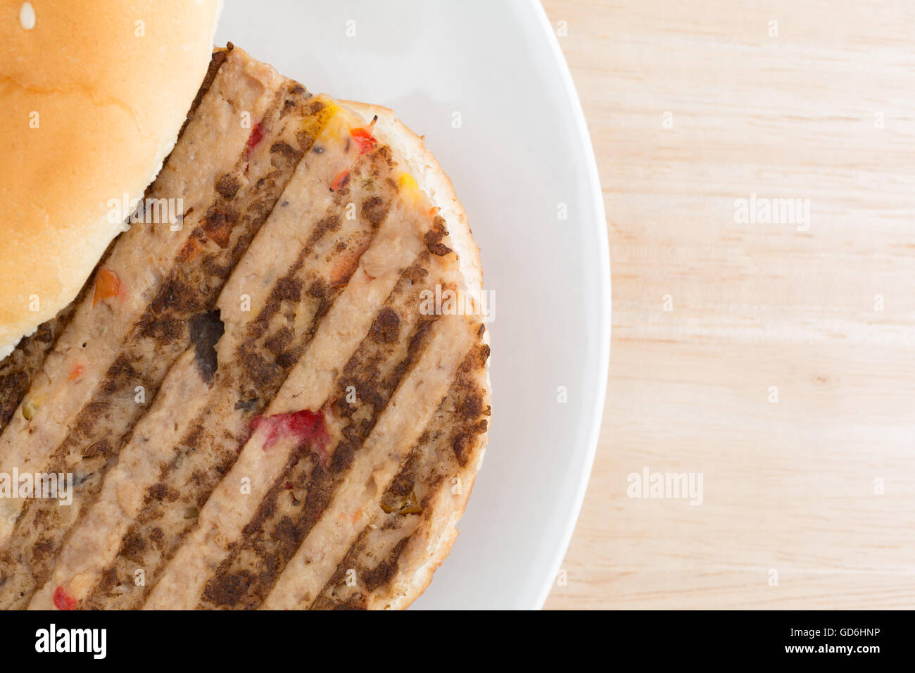 Top vista ravvicinata di un hamburger vegetariano in un panino con condimenti non su una piastra in cima a una tavola di legno alto. Foto Stock