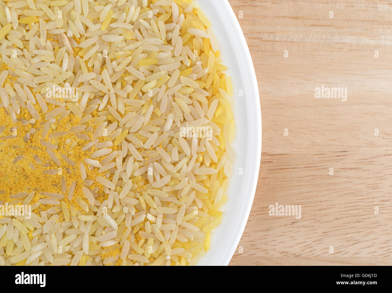 Top vista ravvicinata di zafferano riso e condimenti su una piastra bianca in cima a una tavola di legno. Foto Stock