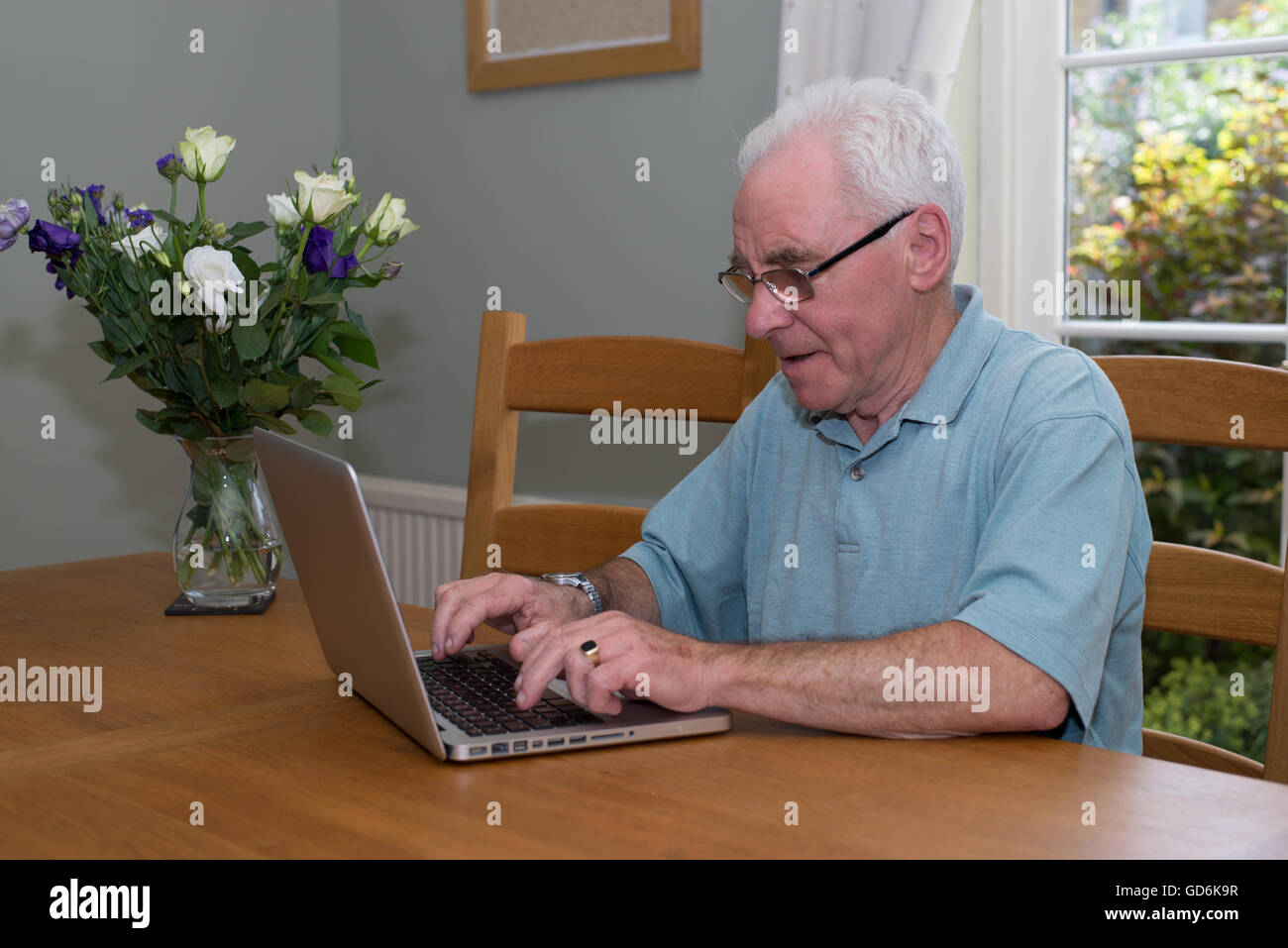 Il vecchio uomo seduto a una tavola utilizzando un computer portatile Foto Stock