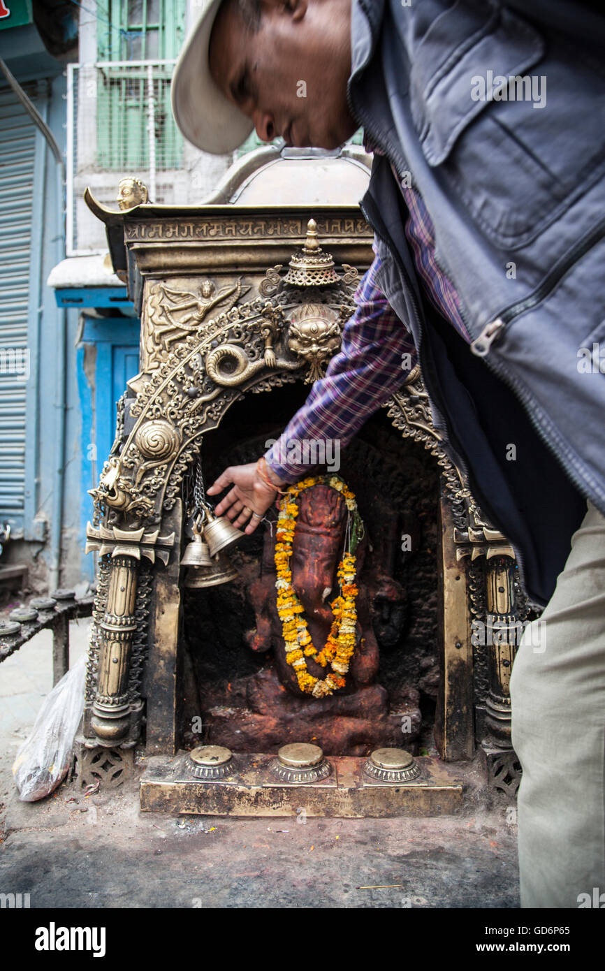 Uomo nepalese trovando conforto in adorando dio elefantino Ganesh. Perso case ma non perdere la fede in lui. Foto Stock