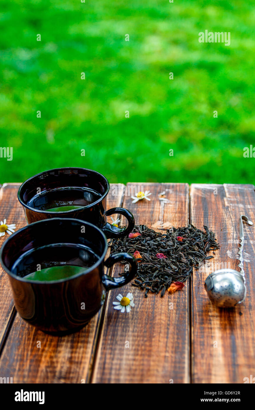 2 tazza di tè nei pressi di foglie secche di tè nero fare nel cuore, vicino Vintage filtro sul tavolo di legno in giardino e sulla natura backgro Foto Stock