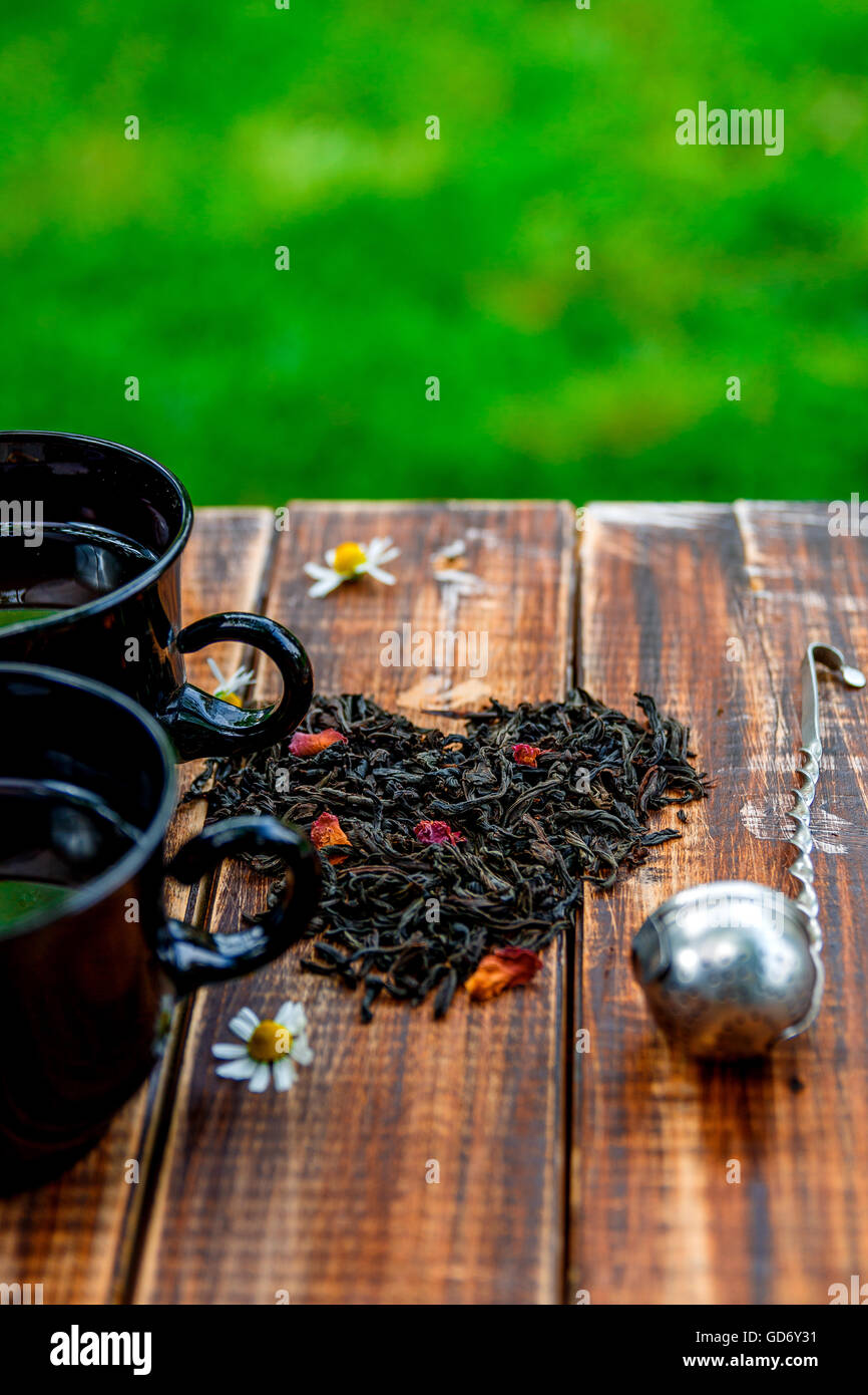 2 tazza di tè nei pressi di foglie secche di tè nero fare nel cuore, vicino Vintage filtro sul tavolo di legno in giardino e sulla natura backgro Foto Stock