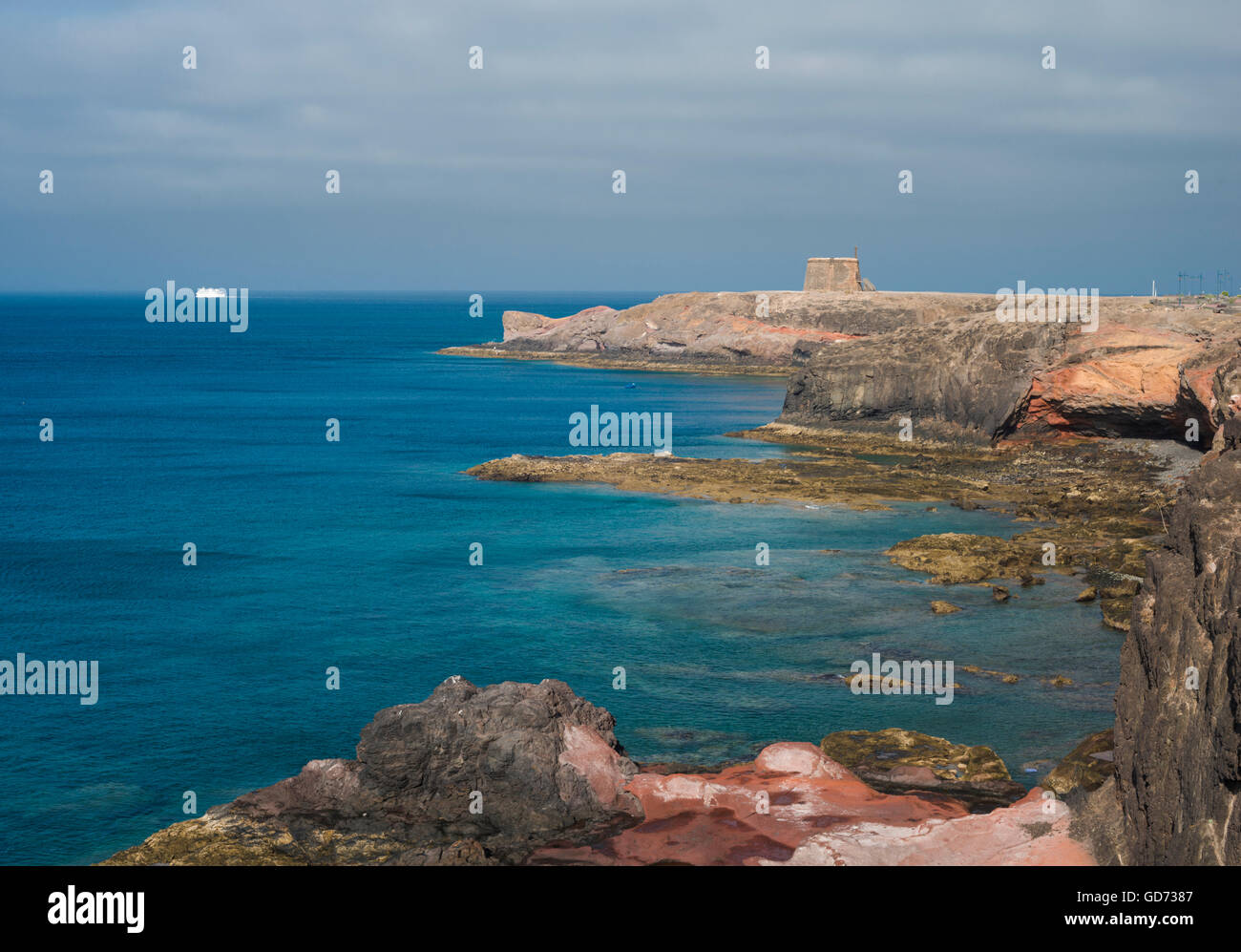 Vista lungo la costa dalle scogliere a est di Playa Blanca, Lanzarote, con il traghetto per Fuerteventura in distanza Foto Stock