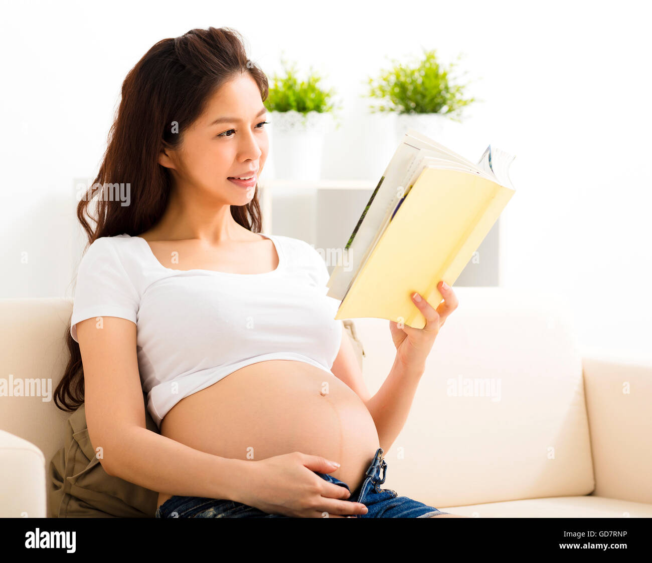 Donna incinta in appoggio a casa e la lettura di un libro sul divano Foto Stock