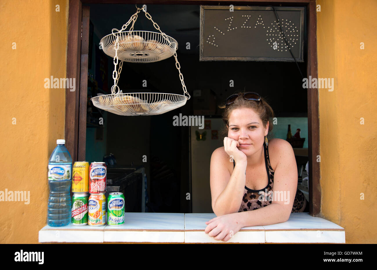 Una giovane donna cubana si appoggia attraverso il portello della sua cucina pizza in Trinidad, Cuba Foto Stock