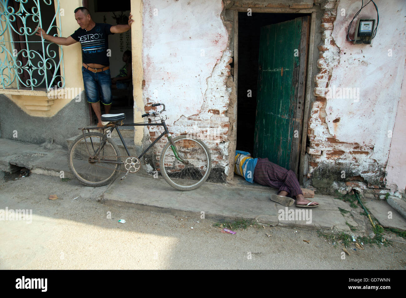 Un cubano uomo giace ubriaco e addormentato nella porta di ingresso per la sua fatiscente casa in un quartiere povero di Trinidad, Cuba Foto Stock