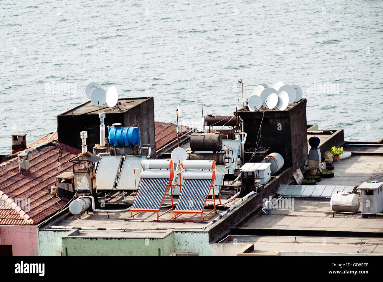 Una vista dal tetto sul mare con pannelli solari, parabole satellitari e serbatoi d'acqua mette in mostra soluzioni tecnologiche urbane per l'energia e la comunicazione Foto Stock