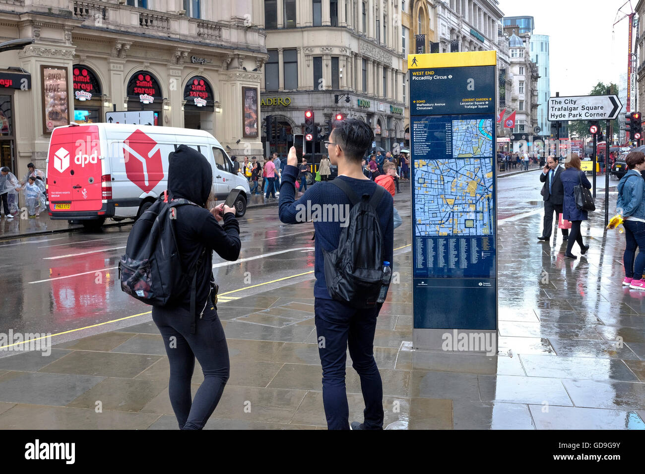 Piccadilly Circus di Londra. Un turista cinese prende una fotografia di Eros con il suo smart phone su un umido e giorno di pioggia a Piccadilly Circus Londra Foto Stock