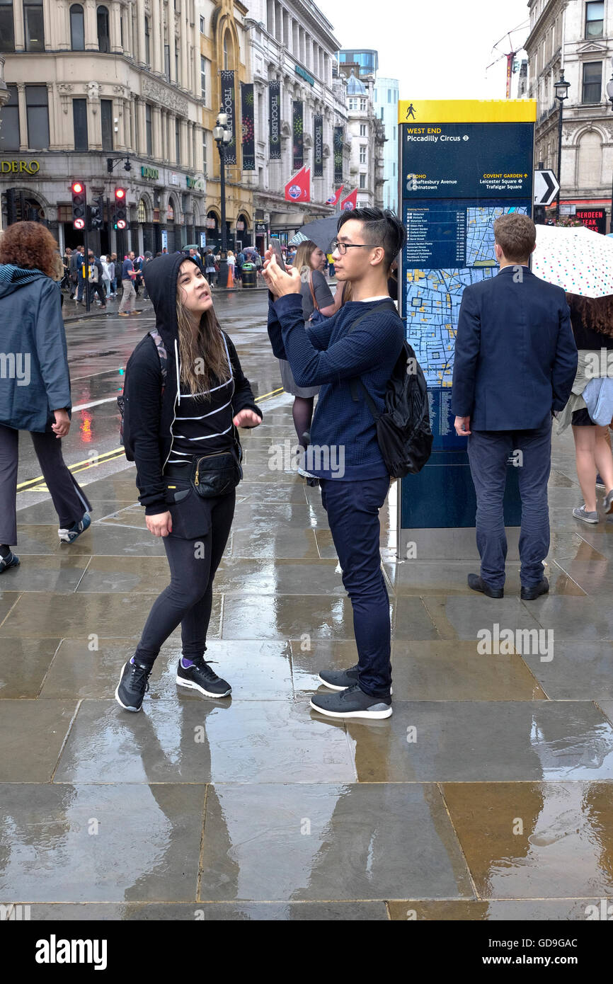 Piccadilly Circus di Londra. Un turista cinese prende una fotografia di Eros con il suo smart phone su un umido e giorno di pioggia a Piccadilly Circus Londra Foto Stock
