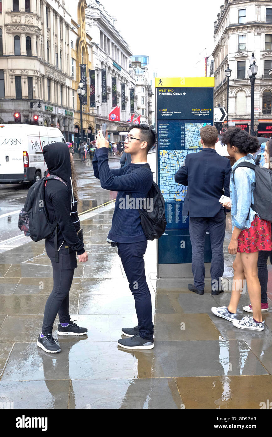 Piccadilly Circus di Londra. Un turista cinese prende una fotografia di Eros con il suo smart phone su un umido e giorno di pioggia a Piccadilly Circus Londra Foto Stock