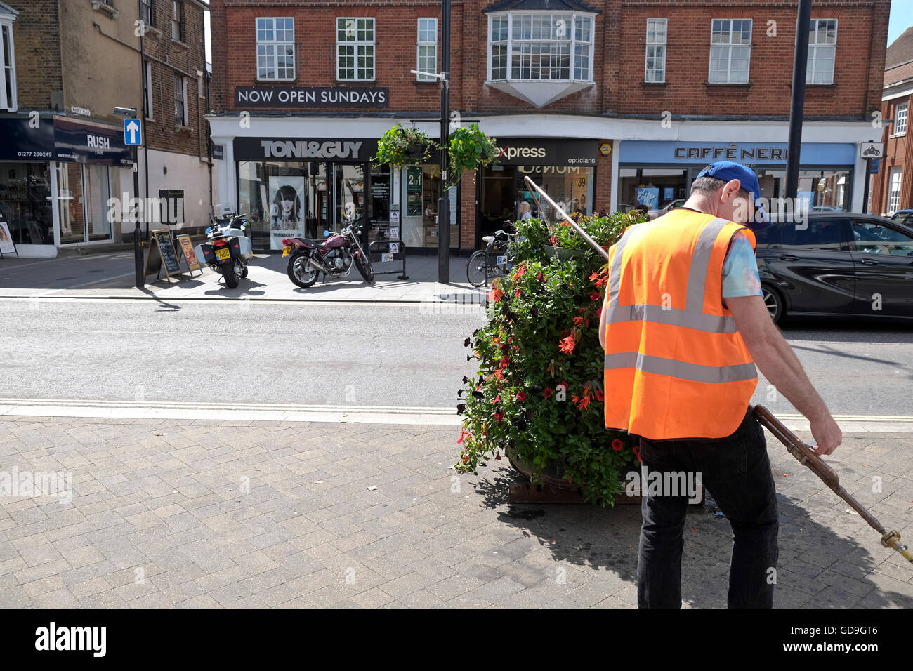 Un lavoratore del consiglio acque fiori sulla Strada Alta di Brentwood una piccola cittadina inglese in Essex Foto Stock