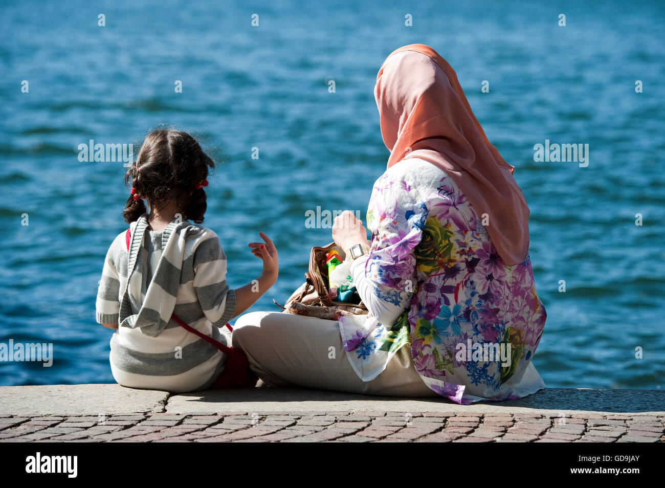 Donna con velo e figlia seduti su un lago Foto Stock