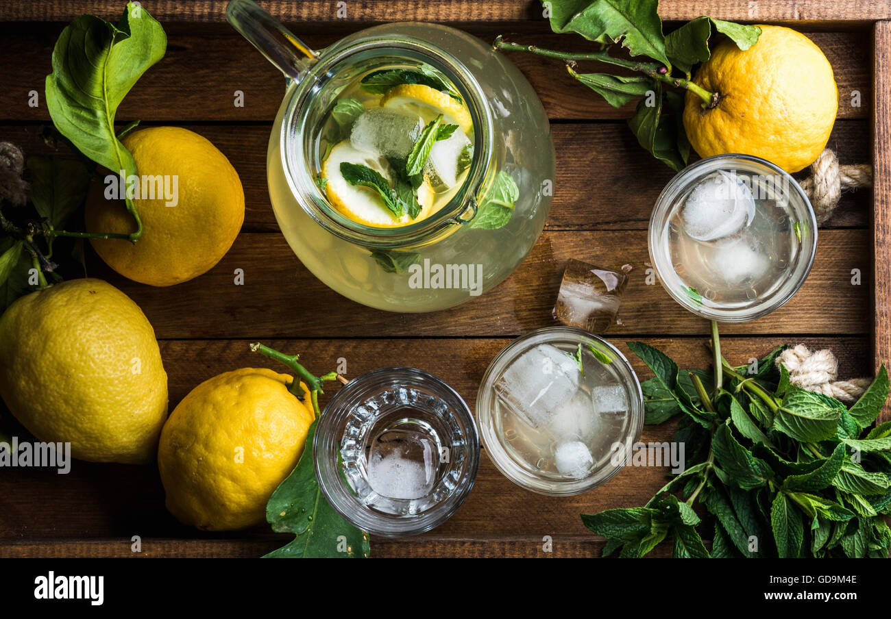 Limonata fatta in casa con la menta, ghiaccio e limoni freschi serviti con limoni freschi e menta sul vassoio in legno sfondo, vista dall'alto Foto Stock