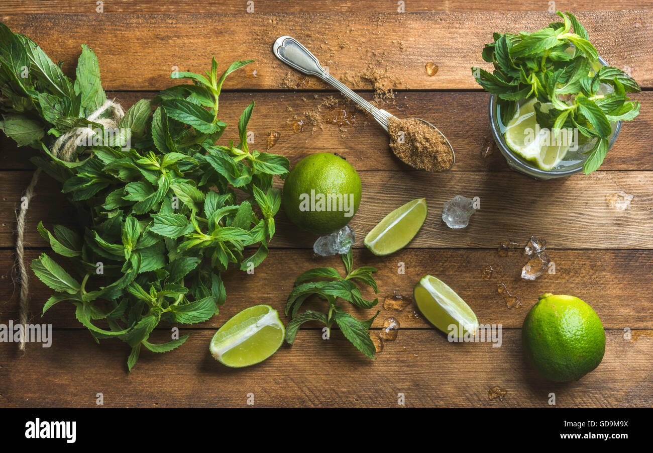 Ingredienti per rendere mojito summer cocktail. Di menta fresca mazzetto, tigli, lo zucchero di canna e ghiaccio su legno rustico sfondo, top v Foto Stock