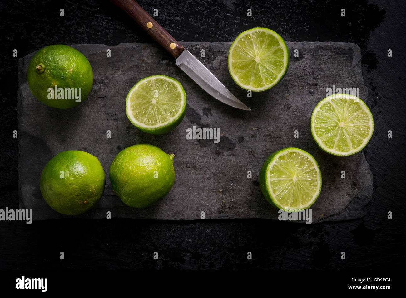 Intero e tagliare limes sul nero ardesia bordo con coltello vintage. Vista dall'alto. Foto Stock