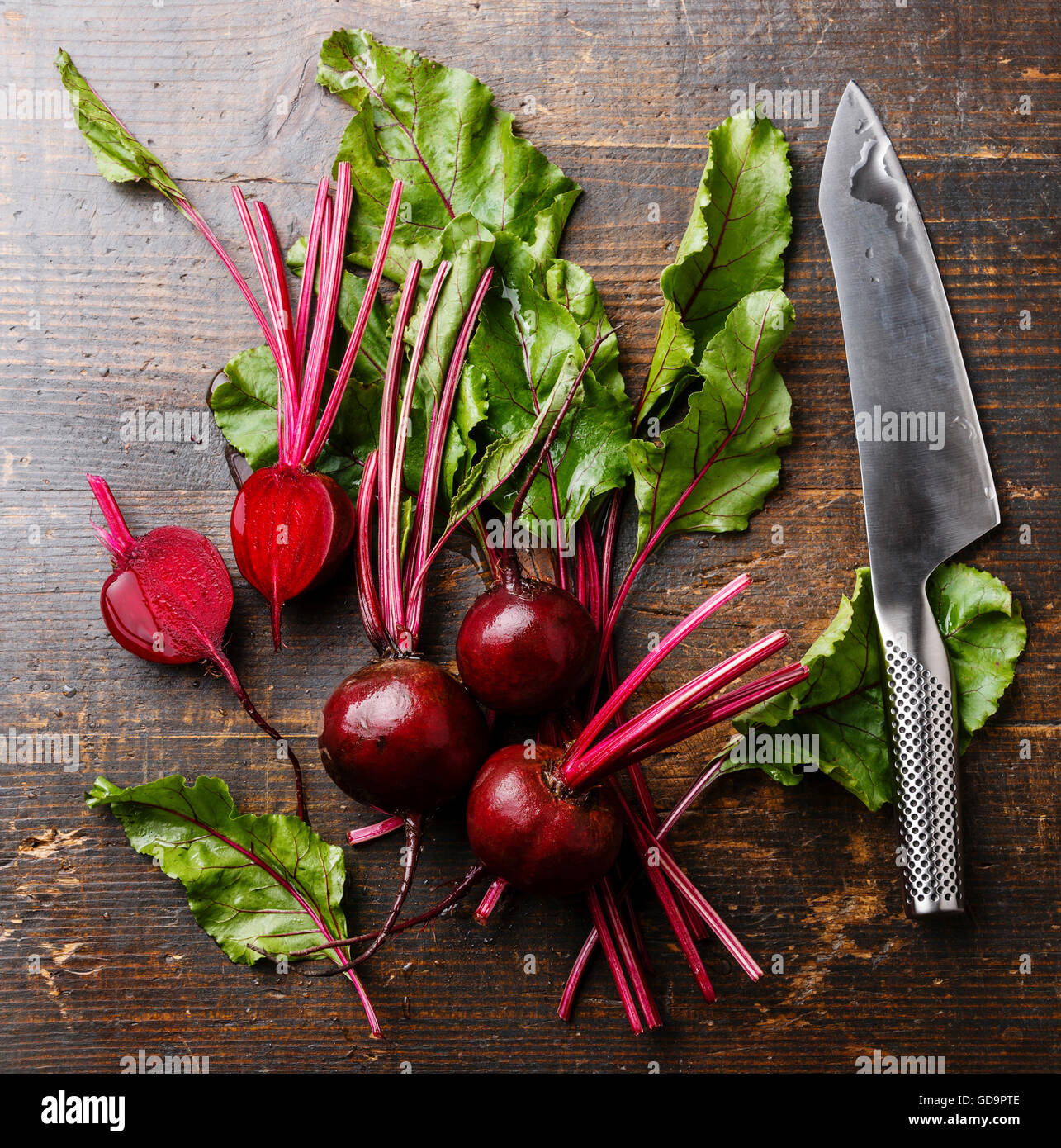 La barbabietola rossa con herbage foglie verdi e coltello da cucina su sfondo di legno Foto Stock